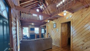 A log cabin interior with a wooden floor, a sofa, a fireplace, and a ceiling fan. - Mountain Rose- Hot Tub, Pool Table, Firepit, Fireplace (Stanton)