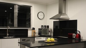 A modern kitchen with a black countertop, stainless steel appliances, and a window with blinds. - Orchard Leigh on the Quarry (Dunedin)