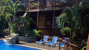 Una piscina con borde de azulejos, rodeada de sillas de descanso y plantas tropicales.