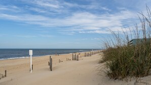 Ein Strand mit Holzlattenzaun, einem Schild und hohem Gras.