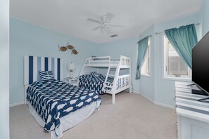 A bedroom with two beds, a ceiling fan, a TV, and a window with curtains.