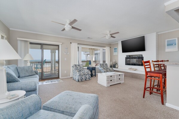 A spacious living room with a flat-screen TV, ceiling fans, and a dining area with wooden chairs.