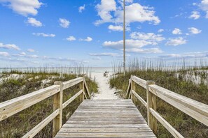 Un muelle de madera que conduce a una playa con arena y vegetación escasa.