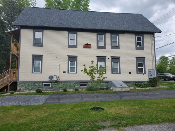 A two-story building with a balcony on the second floor, a small tree in front, and a car parked nearby. - Contemporary king w/futon (Whitehall)