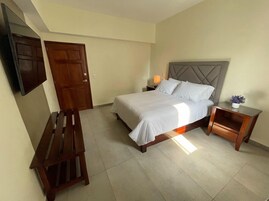 A hotel room with a bed, a wooden bench, a nightstand, and a wall-mounted TV.