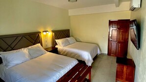 Una habitación de hotel con dos camas, un banco de madera, un armario y una lámpara en el techo.
