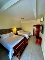 A hotel room with two beds, a wooden bench, a wardrobe, and a ceiling light.