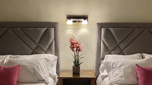 Una habitación de hotel con dos camas, una mesita de noche con un florero y una lámpara de pared.