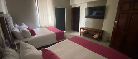 Habitación de hotel con dos camas, un televisor, un banco de madera y una puerta.