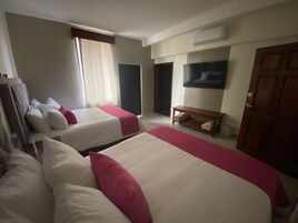 A hotel room with two beds, a TV, a wooden bench, and a door.