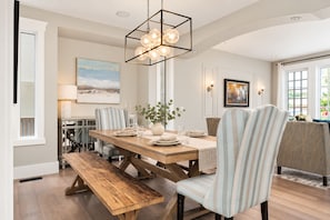 A dining area with a wooden table, striped chairs, a bench, and a hanging light fixture.