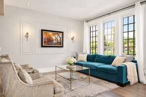 Ein modernes Wohnzimmer mit einem petrolfarbenen Sofa, einem Ohrensessel mit Marmormuster und einem Glastisch.
