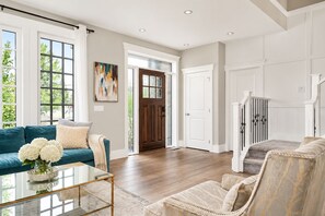 A spacious living room with a blue sofa, a glass coffee table, and a beige armchair.