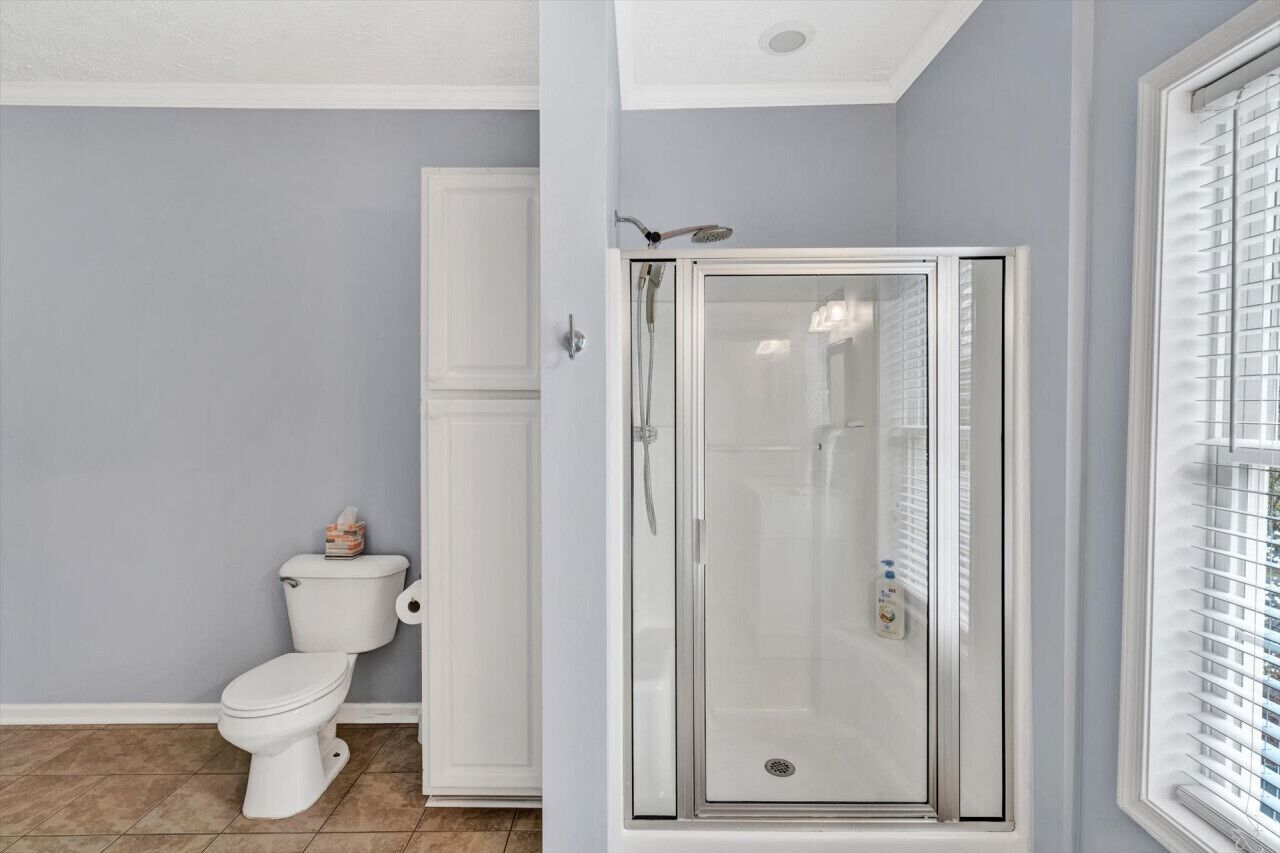 A bathroom with a toilet, a shower enclosure, and a window with blinds.
