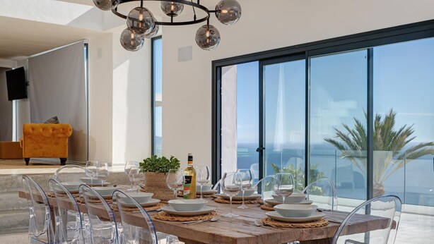 A dining area with a wooden table, clear chairs, and a view of the ocean. - Luxury villa, breathtaking views and heated pool (Salobreña)