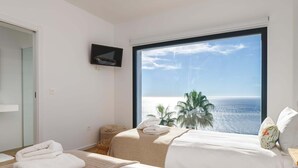A hotel room with a large window, a flat-screen TV, two beds, a small table, and a view of the sea. - Luxury villa, breathtaking views and heated pool (Salobreña)