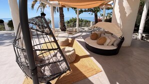 A covered outdoor seating area with a swing chair, cushioned seating, and a view of the sea. - Luxury villa, breathtaking views and heated pool (Salobreña)