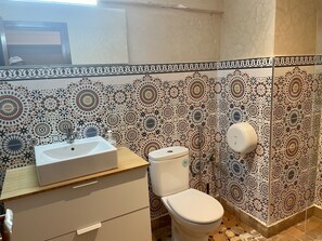 Un bany amb rentapel, vàter i plat de dutxa. Les parets estan decorades amb rajoles amb dibuixos.