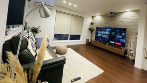 Un saló modern amb un televisor de pantalla plana gran, un sofà de cuir negre, una catifa blanca i un paviment de fusta.
