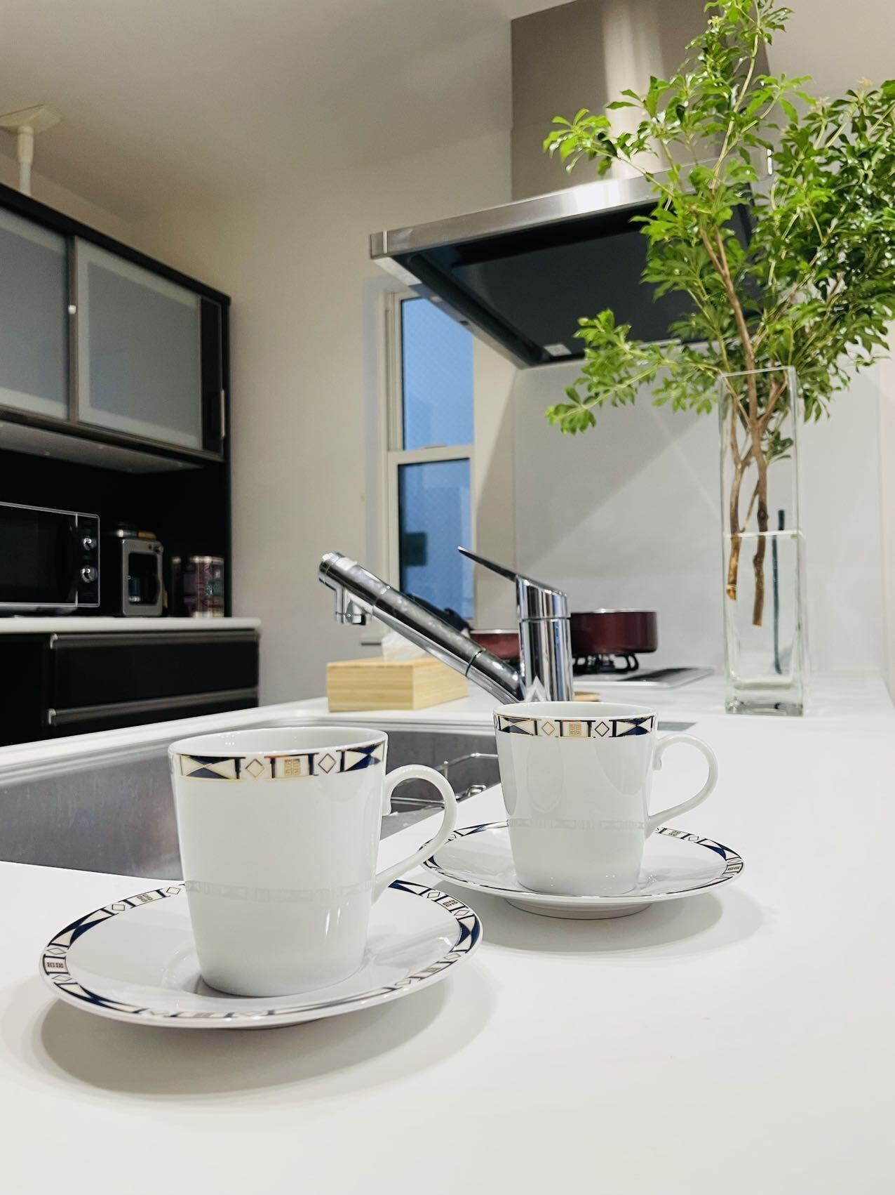A modern kitchen with two white cups on a white tray, a stainless steel faucet, and a potted plant.
