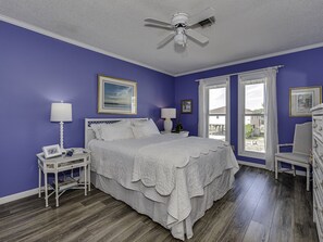 A bedroom with a bed, two bedside tables, a nightstand, a ceiling fan, and a window with curtains. - Recently Renovated Canal Home in OIB bring your boat or just float ! (Ocean Isle Beach)