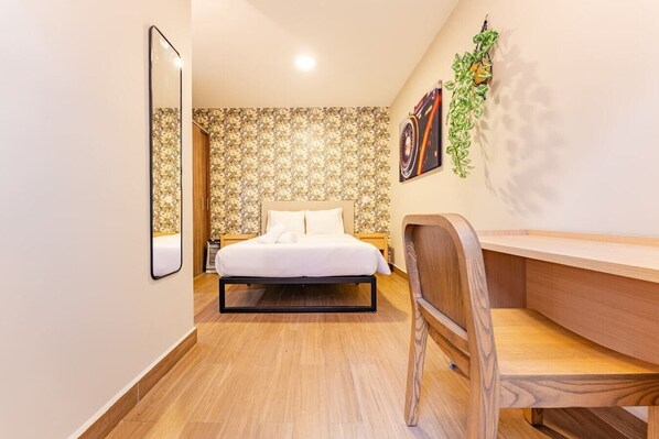 Cozy retreat with a neatly made bed, wooden desk, and a small bedside table.