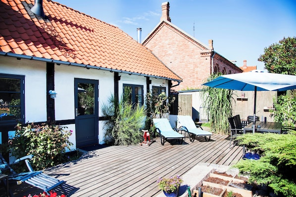 A wooden deck with lounge chairs, a barbecue area, and a large umbrella.