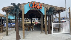 Ein Restaurant direkt am Strand namens 'Oasis' mit Außenbereich und Palmen.