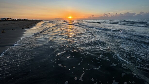 Ein Strand bei Sonnenuntergang mit Wellen.