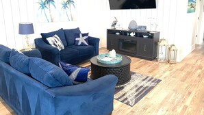 Ein Wohnzimmer mit einem dunkelblauen Sofa, einem Couchtisch und einem flachbildfernseher an der Wand.
