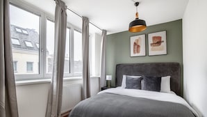 A bedroom with a large bed, a radiator, a window with curtains, and two abstract paintings on the wall. - Premium Hernals 1BR w/ Balcony, nr Lidlpark, by Blueground (Vienna)