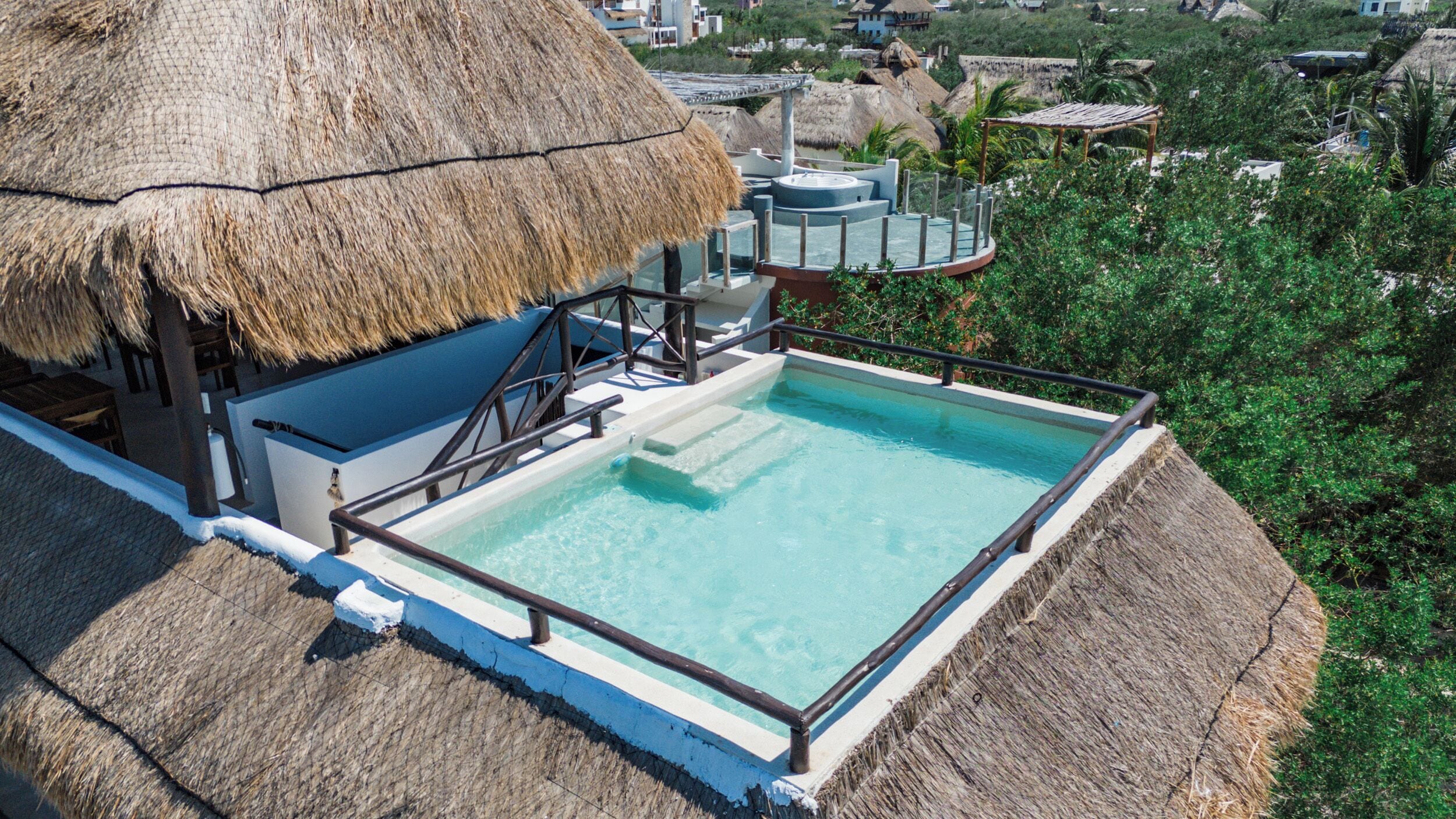 Una piscina con una estructura de techo de paja, rodeada de exuberante vegetación.