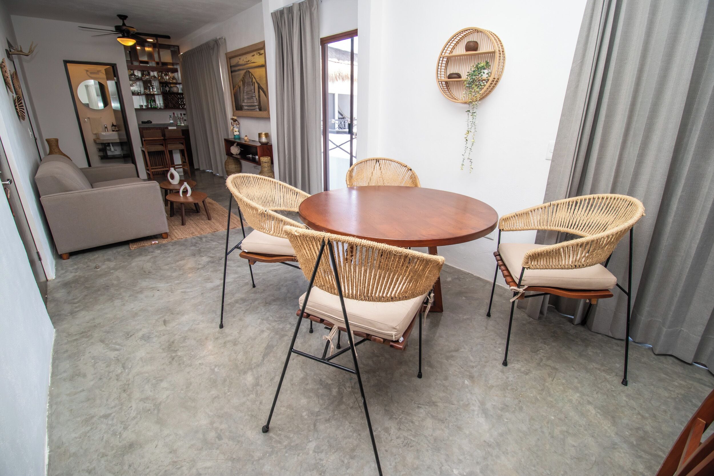 A dining area with a round wooden table and four wicker chairs with cushions.