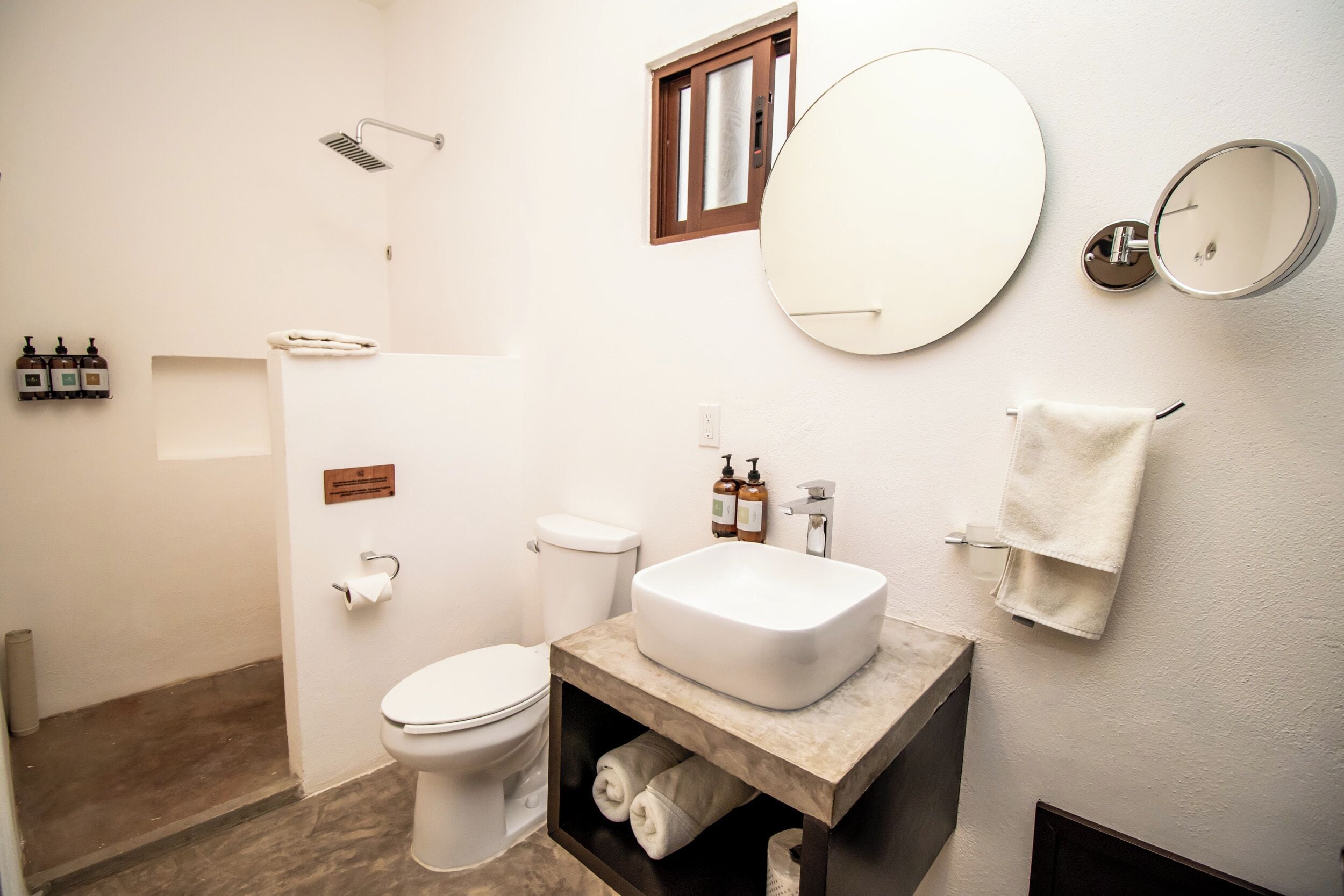 Un baño con inodoro blanco, lavamanos con encimera de mármol, ducha y espejo.