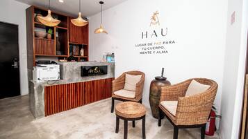 A reception area with wicker chairs, a reception desk, and a wall with the hotel name and slogan.