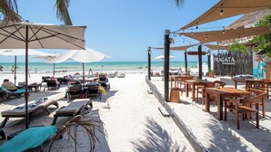 Un restaurant situé en bord de mer, avec une terrasse comprenant des tables, des chaises et des parasols pour offrir de l’ombre.