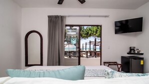 Une chambre d’hôtel avec un lit, une télévision, un petit bureau et un balcon donnant sur la mer.