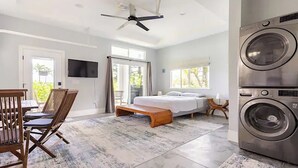 A modern bedroom with a bed, a washing machine, and a dining area with chairs. - Two homes on the ocean with a private saltwater pool.  (Keaau)