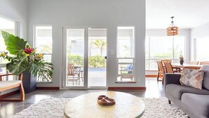 A spacious living area with a round coffee table, a grey sofa, and a large window offering a view of the outdoors. - Two homes on the ocean with a private saltwater pool.  (Keaau)