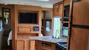 Una cuina d'autocaravana compacta amb armaris de fusta, fogó integrat, microones i televisió.