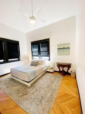 Cozy retreat with a bed, bedside table, and nightstand, set against a large window with a painting above.