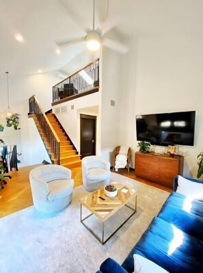 Relax in this spacious living room with a large flat-screen TV, comfortable seating, and a wooden staircase leading to the upper level.