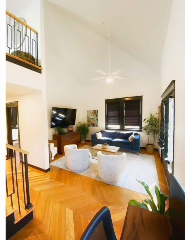 Relax in this spacious living area with a high ceiling, featuring a large flat-screen TV and comfortable sofa.