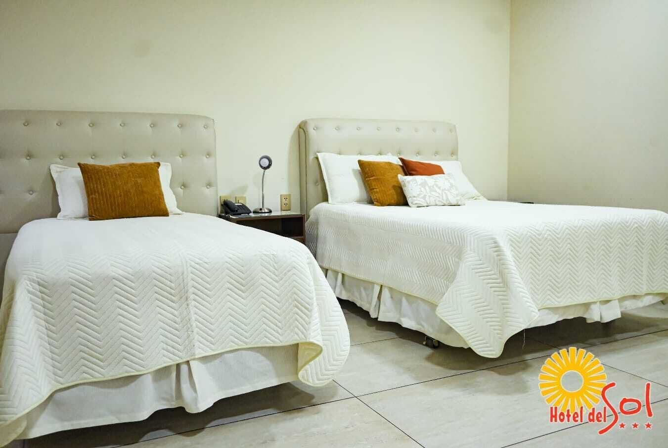 Two single beds with white bedding and brown pillows, a bedside table with a phone, and a light-colored wall.