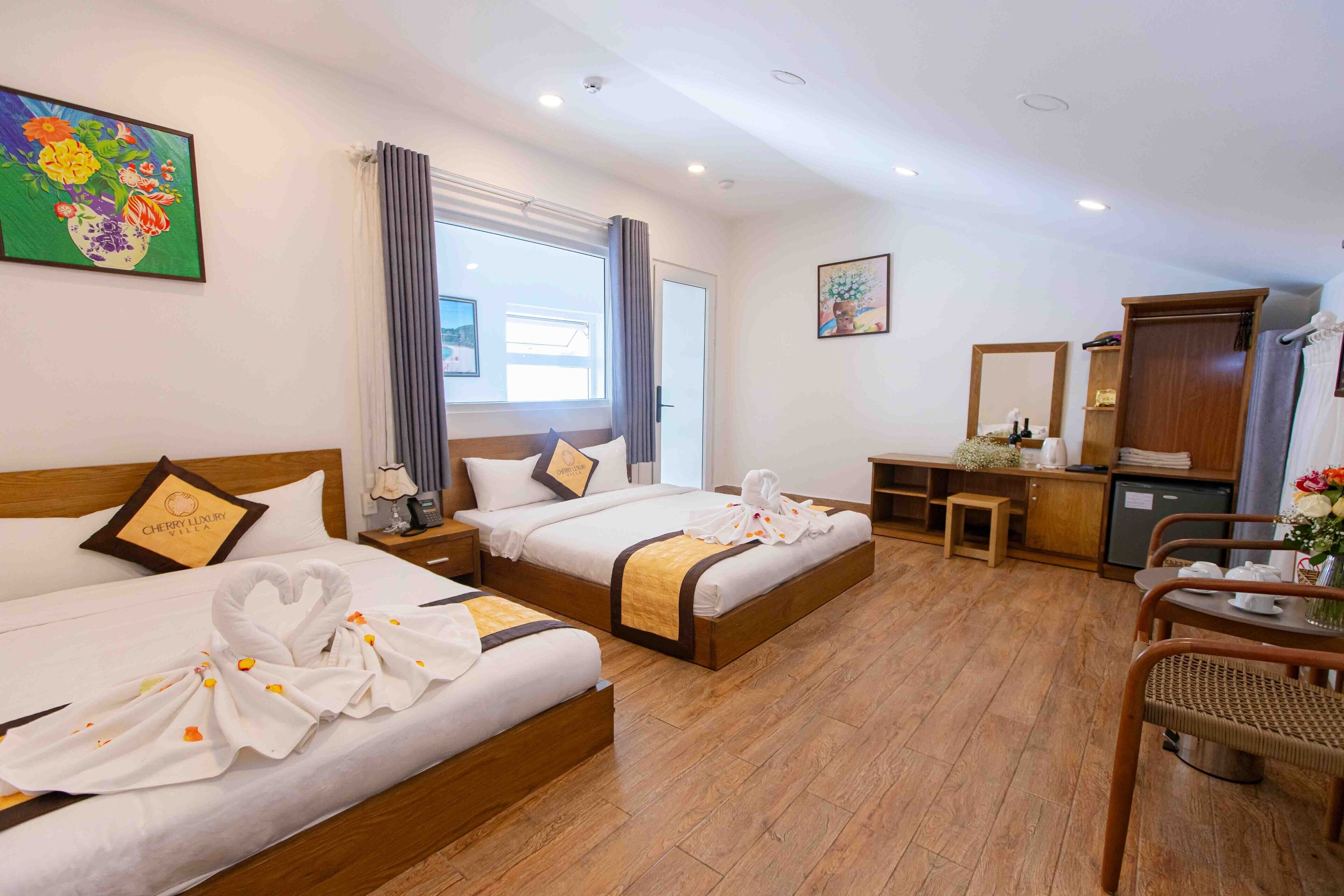 A hotel room with two beds, a desk, a chair, a small table, and a bathroom.