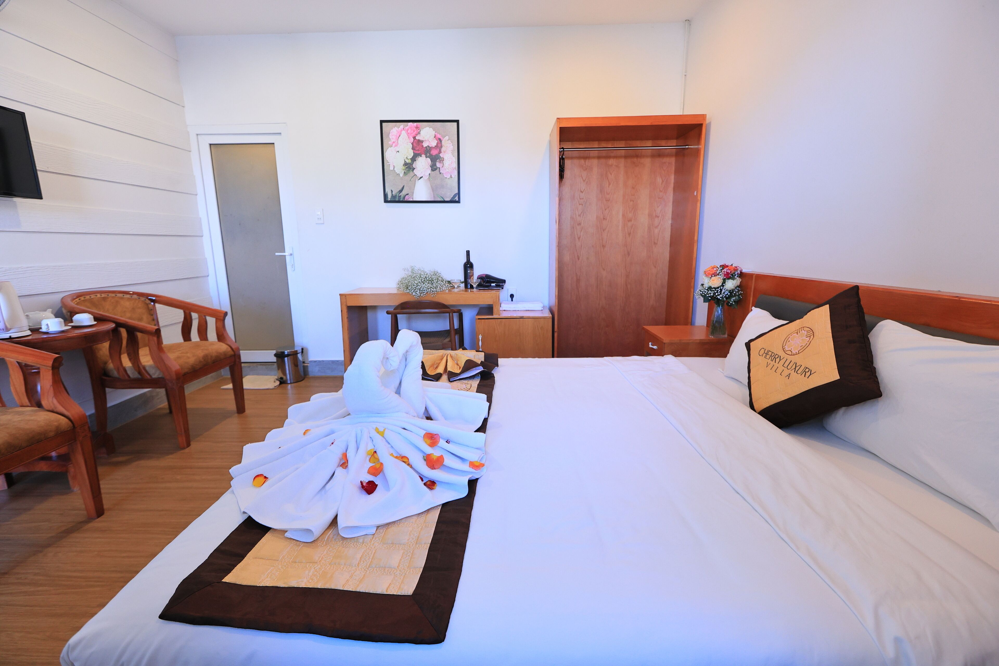 A hotel room with a bed, a desk, a chair, a TV, and a door.