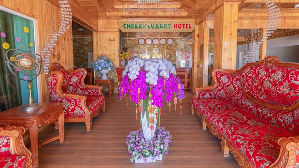 A hotel lobby with wooden paneling, red upholstered sofas, a chandelier, and a floral centerpiece. - Cherry Luxury Hotel (Xuan Huong - Da Lat)
