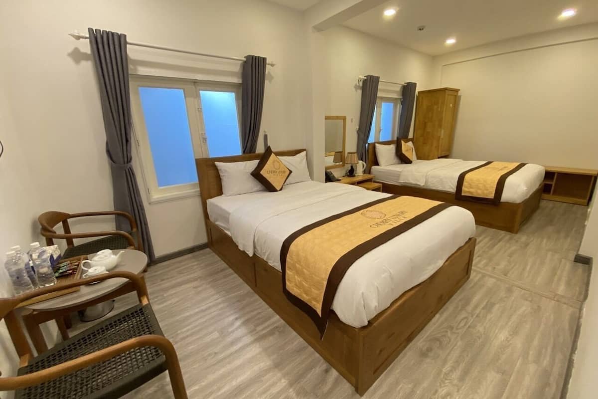 A hotel room with two beds, a desk with chairs, a mirror, and a wardrobe.