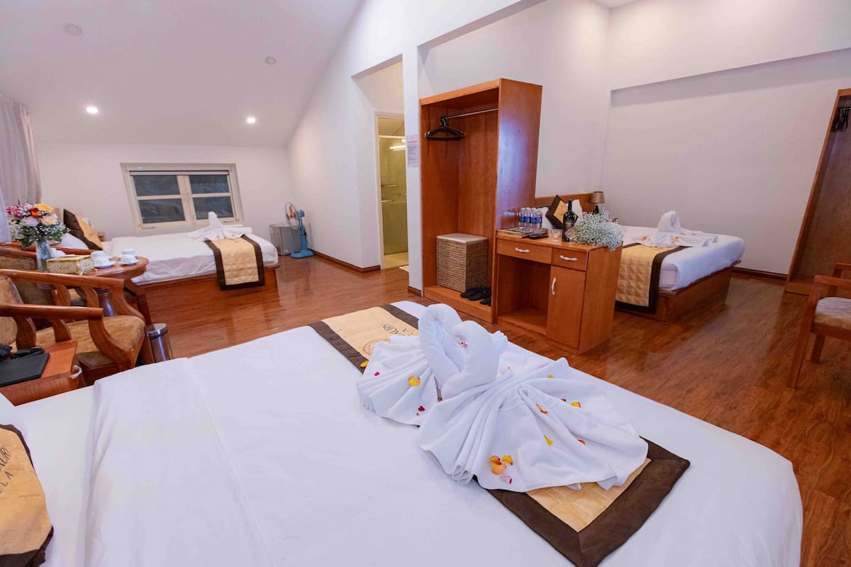 A hotel room with two beds, a wooden wardrobe, a desk with a chair, and a small bathroom area.