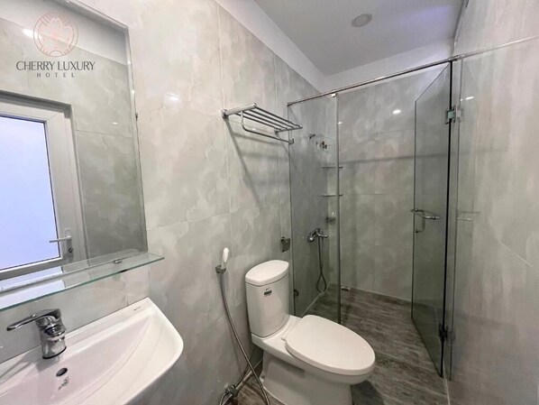 A modern bathroom with a glass shower enclosure, a white sink, and a toilet. - Cherry Luxury Hotel (Xuan Huong - Da Lat)